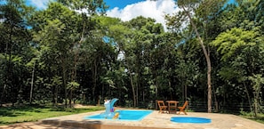 A swimming pool with a slide, surrounded by a fence and trees. - Chácara Lobo - Piscina Aquecida - Pirenópolis/GO (Pirenópolis)