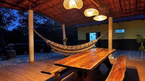An outdoor wooden deck with a hammock, picnic table, and hanging lights.