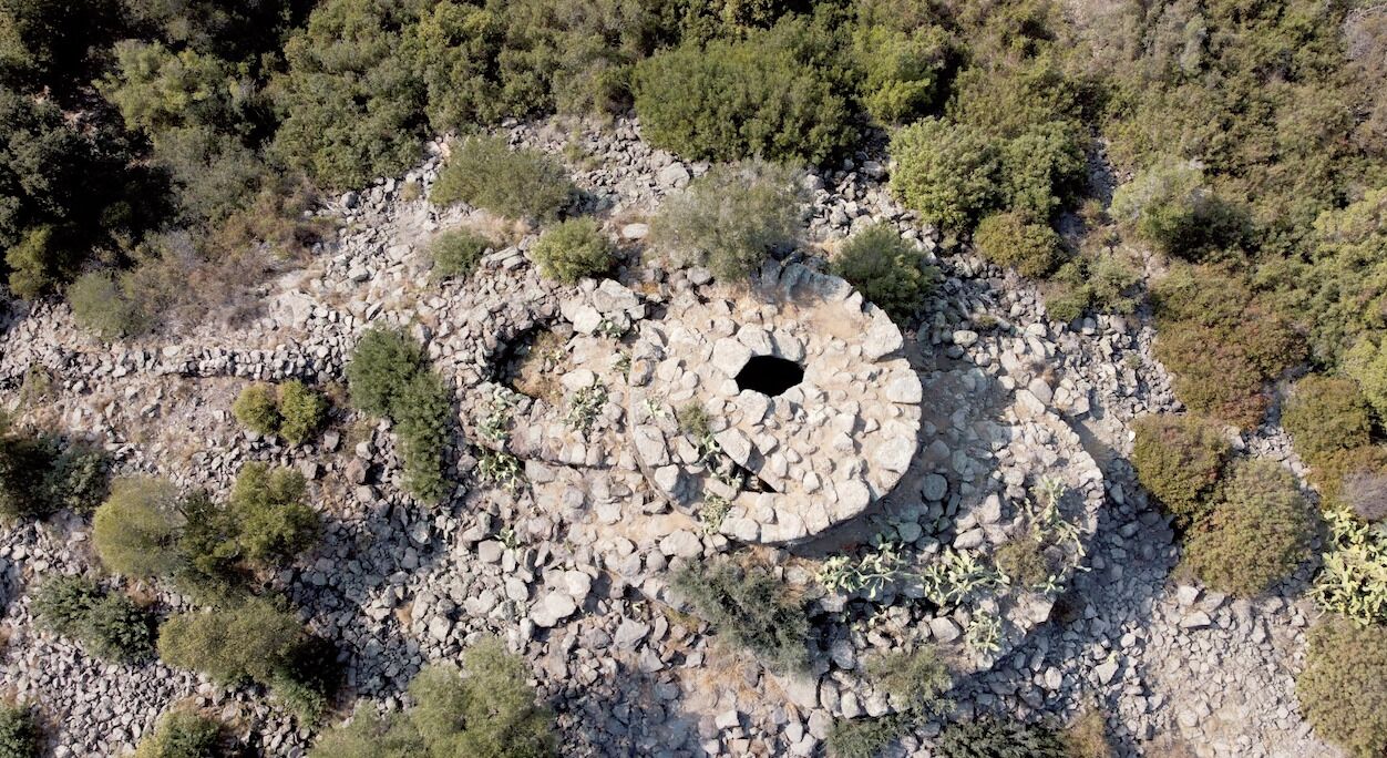 An aerial view of a circular stone structure surrounded by sparse vegetation.