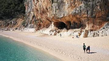 Ein Strand mit klarem türkisblauem Wasser, einer felsigen Klippe und einem Höhleneingang.