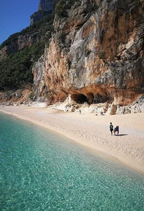 Ein Strand mit klarem türkisblauem Wasser, einer felsigen Klippe und einem Höhleneingang.