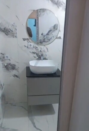 A bathroom with a white sink, a mirror, and a wall with a floral pattern.