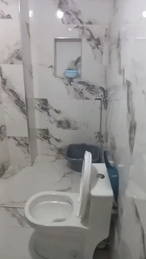 A bathroom with a toilet, a blue basin, and a shower area.