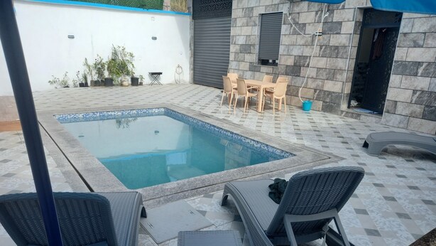 A swimming pool with a tiled deck, surrounded by outdoor furniture and a stone wall.