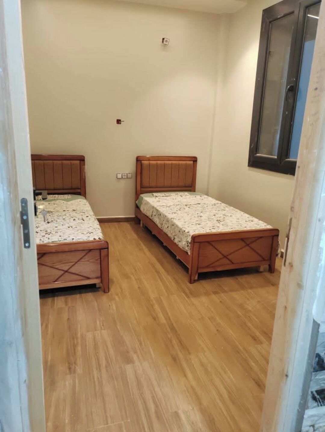 Une pièce avec deux lits en bois, un plancher en bois et une fenêtre.