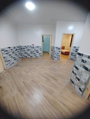 A room with a wooden floor, white walls, and a door leading to another room.