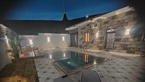 A pool area with a tiled floor, a seating area with chairs, and a wall with decorative lighting.
