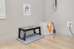 Eine Futterstation für Haustiere mit einem Schild, einem Korb mit Spielzeug und einer Steckdose an der Wand.