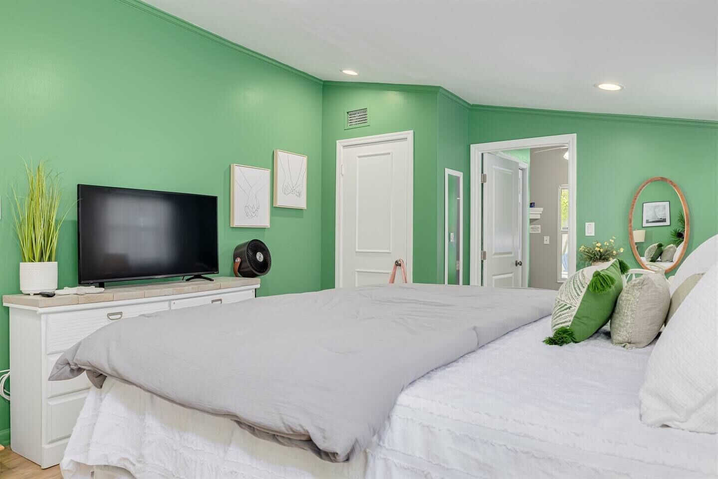 Une chambre à coucher comprenant un lit, un téléviseur, une commode et une porte donnant sur une autre pièce.