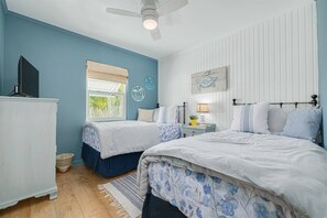 Ein Schlafzimmer mit zwei Betten, einem Deckenventilator, einem Fenster mit Jalousien und einem Wandbild.