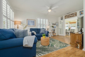 A living room with a blue sofa, a coffee table, and a patterned rug. There is a bookshelf and a dining area visible in the background. - Walk Downtown & Waterfront | Dunedin's Best Street (Dunedin)