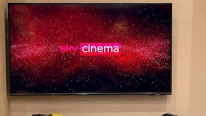 Un televisor con 'sky cinema' en la pantalla, una cafetera, un mini refrigerador con bebidas y una silla.