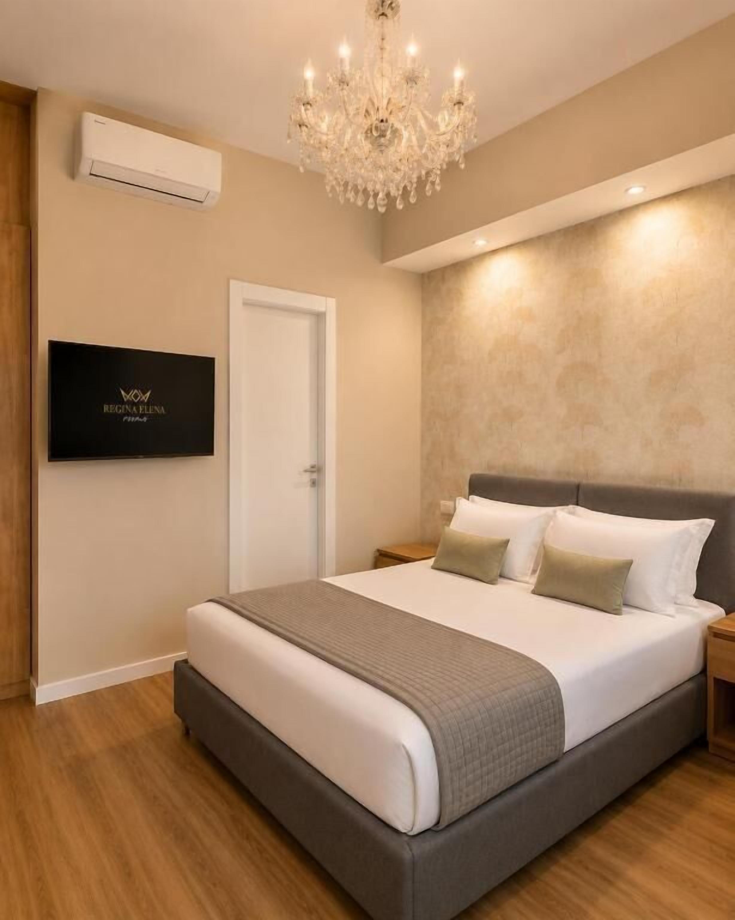 Quarto moderno com cama grande, lustre, televisão e ar-condicionado fixado na parede.
