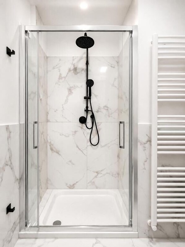 A glass-enclosed shower with a handheld showerhead and a control panel.