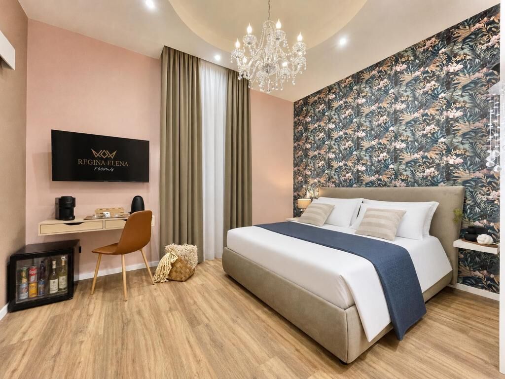 A hotel room with a bed, a desk, a chair, a television, and a chandelier.