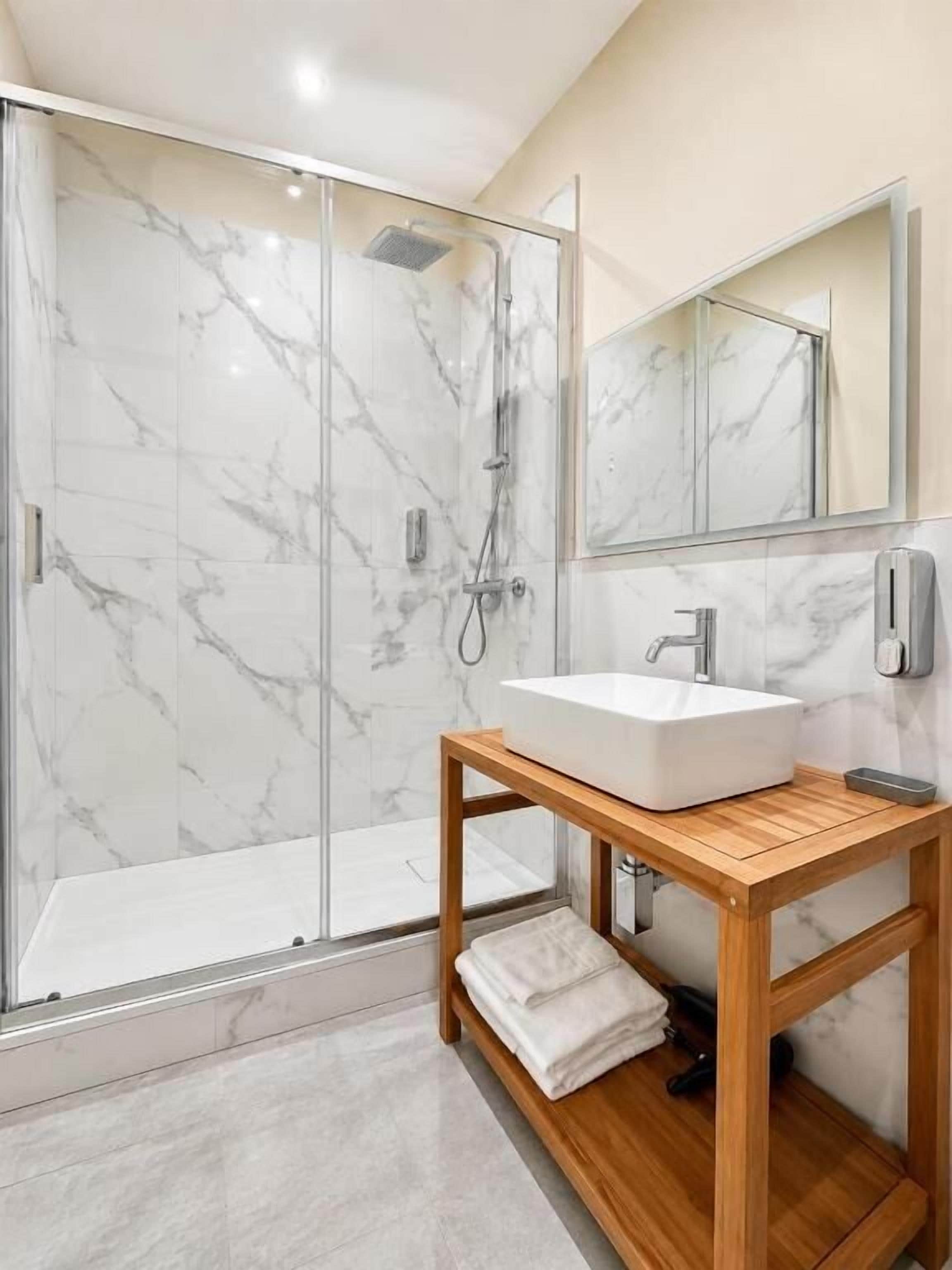 A bathroom with a glass shower enclosure, a wooden vanity with a white sink, and a mirror above the sink.