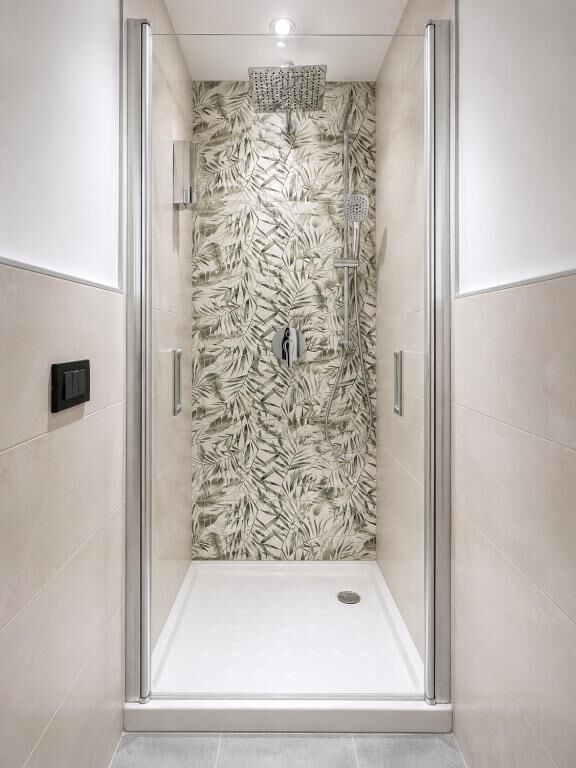 Een moderne douchecabine met een glazen deur en een wand met bladmotief.