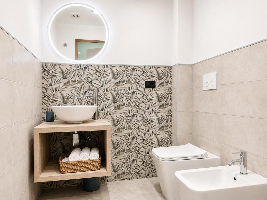 Un baño moderno con un espejo redondo, un lavamanos sobre encimera, un bidé y una bañera.
