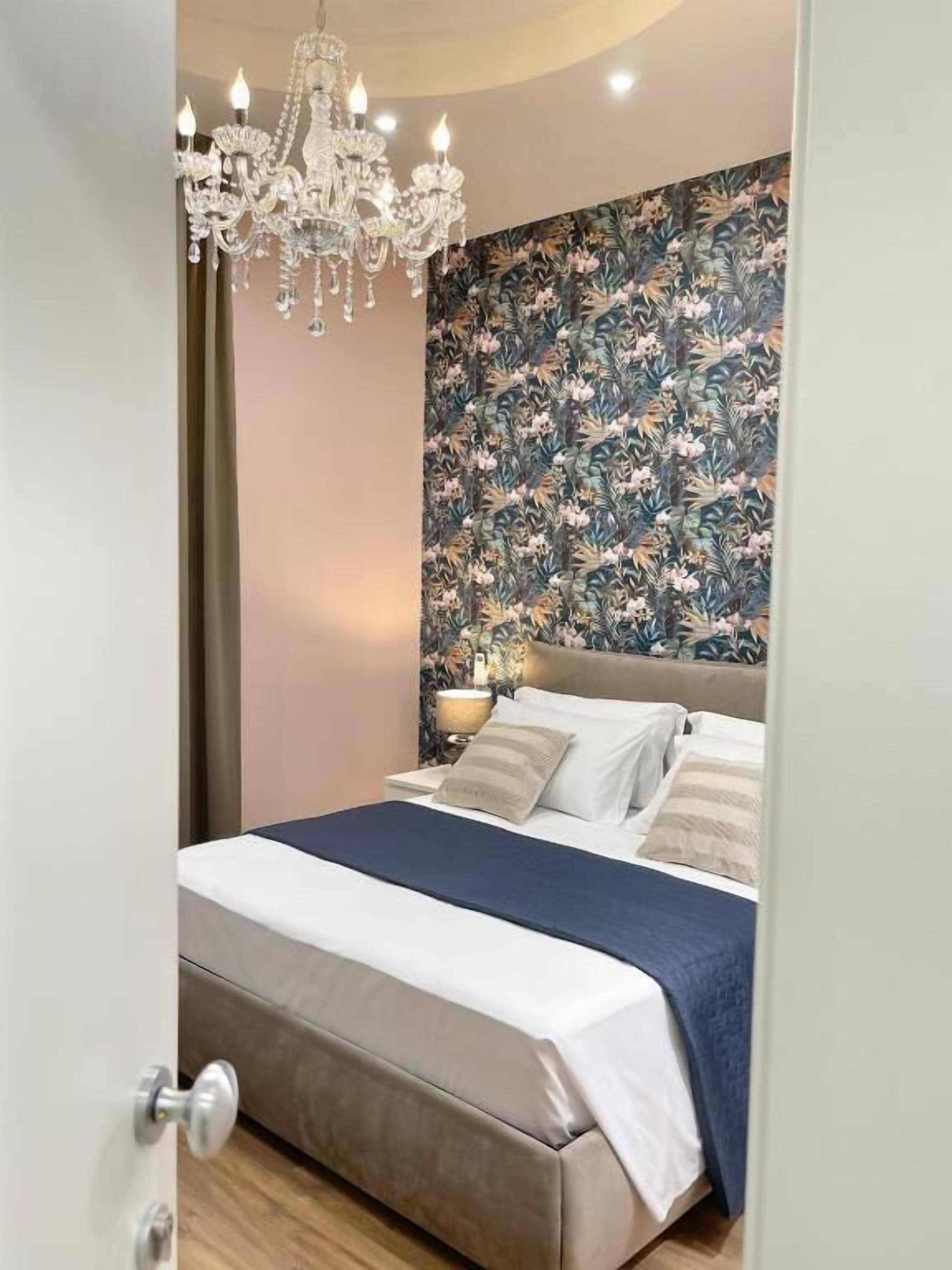 A bedroom with a bed, a chandelier, and a floral wallpaper.