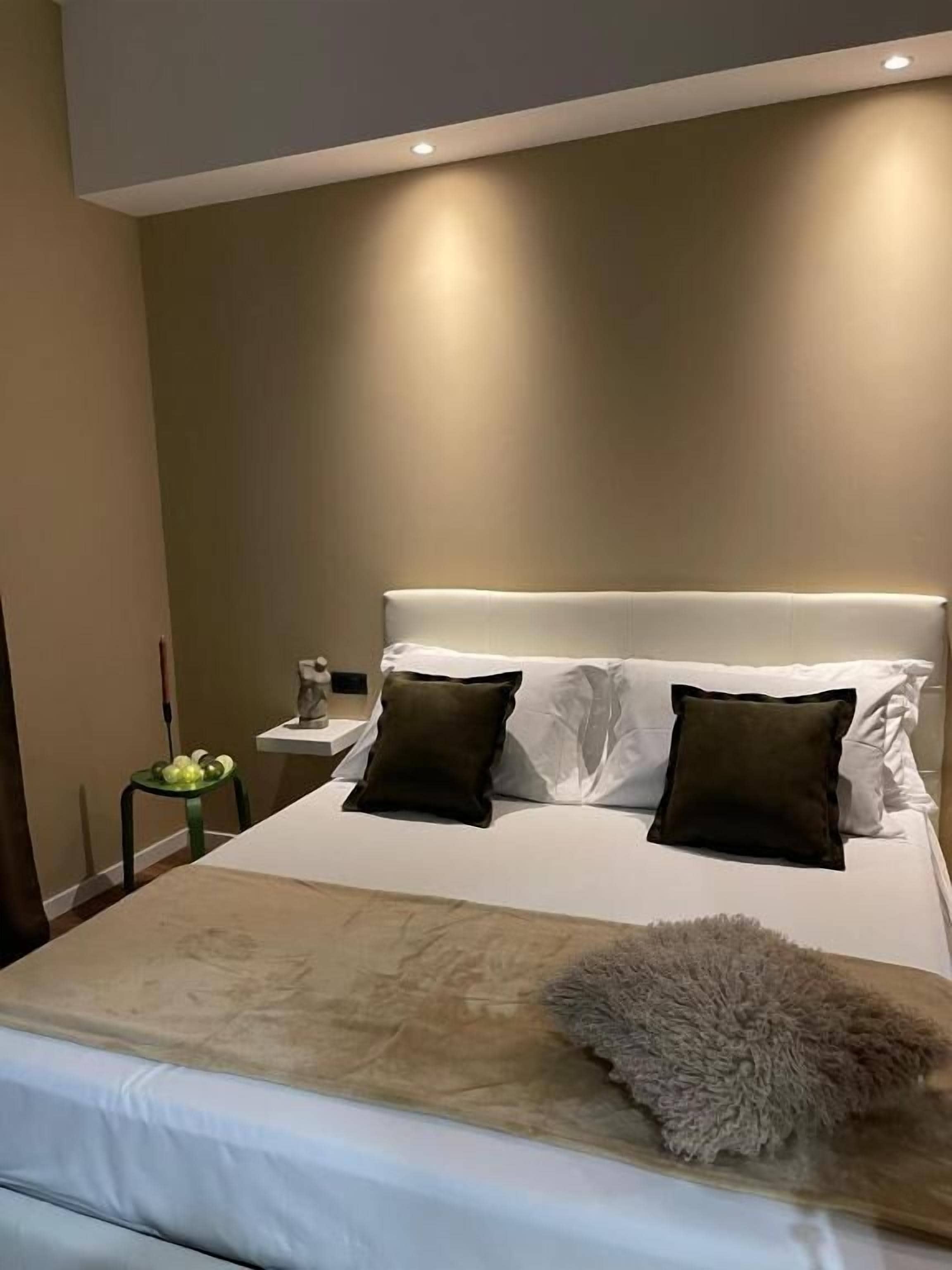 Una cama bien hecha con cabecera blanca, dos almohadas y una manta suave.