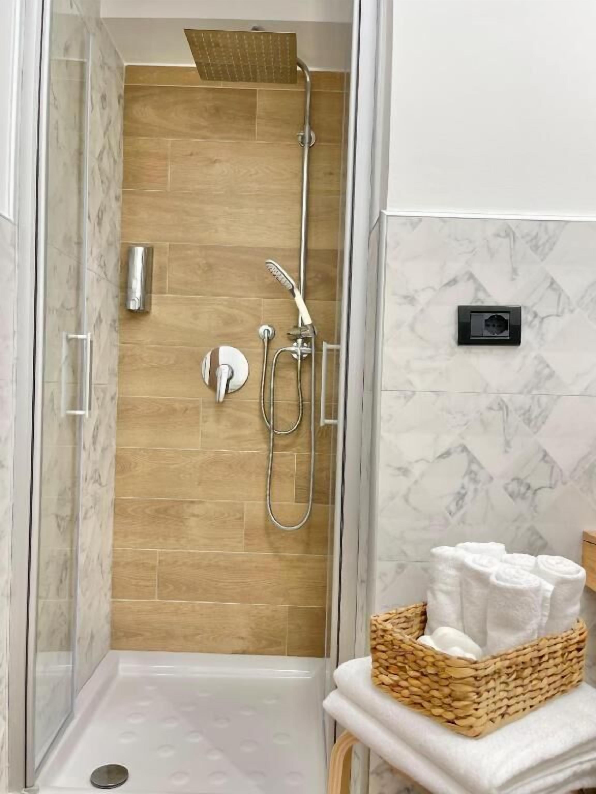 Una doccia con parete in legno, porta in vetro e un cesto di asciugamani su un tavolo.