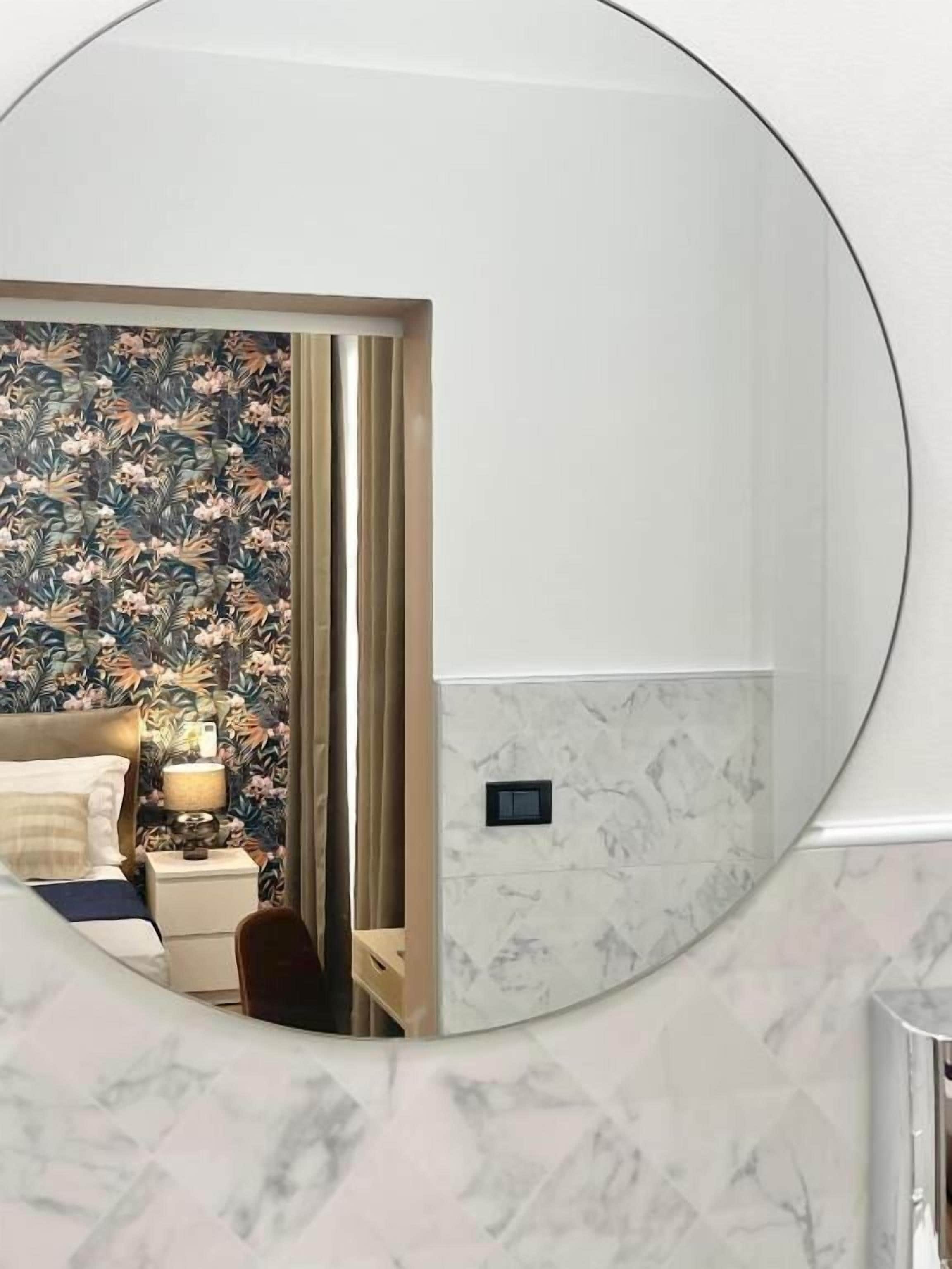 Een hotelkamer met een bed, nachtkastje, lamp en een spiegel die de kamer weerspiegelt.