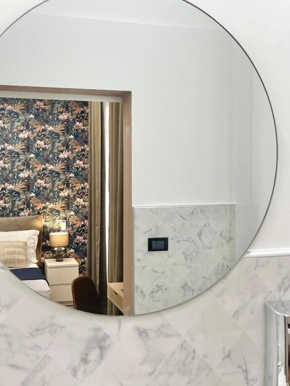 A hotel room with a bed, nightstand, lamp, and a mirror reflecting the room.