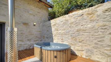 Ein Whirlpool auf einer Holzterrasse mit Steinmauern und einer Metallstange.
