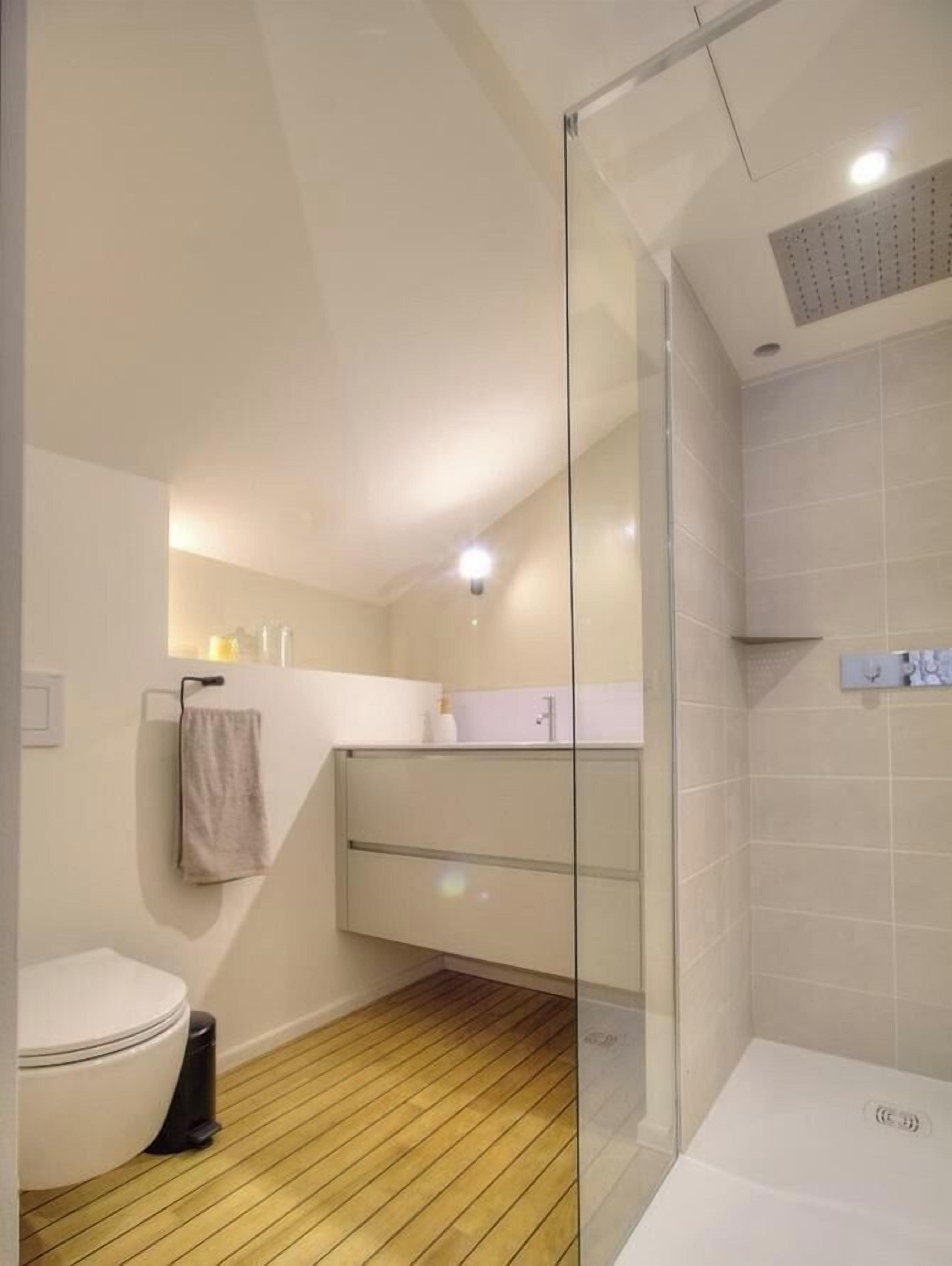 Un bagno moderno con cabina doccia in vetro, un water bianco e un pavimento in legno.