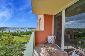 A balcony with a wicker chair and a cushion, overlooking a body of water and greenery. - Modern Bay View Balcony in the Grove Free Parking (Miami)