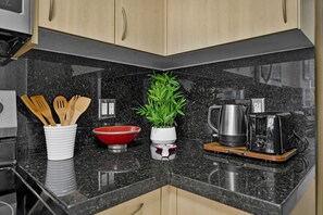 A kitchen counter with a black granite surface, wooden utensils in a white container, a red bowl, a potted plant, a coffee maker, and a toaster. - Modern Bay View Balcony in the Grove Free Parking (Miami)