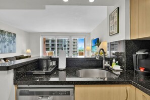 A modern kitchen with a black granite countertop, stainless steel sink, and a built-in dishwasher. - Modern Bay View Balcony in the Grove Free Parking (Miami)