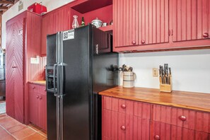 A kitchen with a black refrigerator, red cabinets, and a wooden countertop. - 1844 Alsatian Home on the Medina River (Castroville)