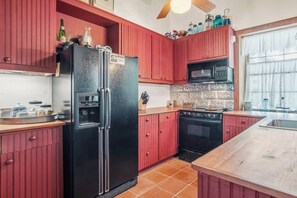 A kitchen with red cabinets, a black refrigerator, a microwave, and a stove. - 1844 Alsatian Home on the Medina River (Castroville)