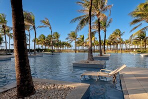 A pool area with palm trees, lounge chairs, and a clear view of the ocean.