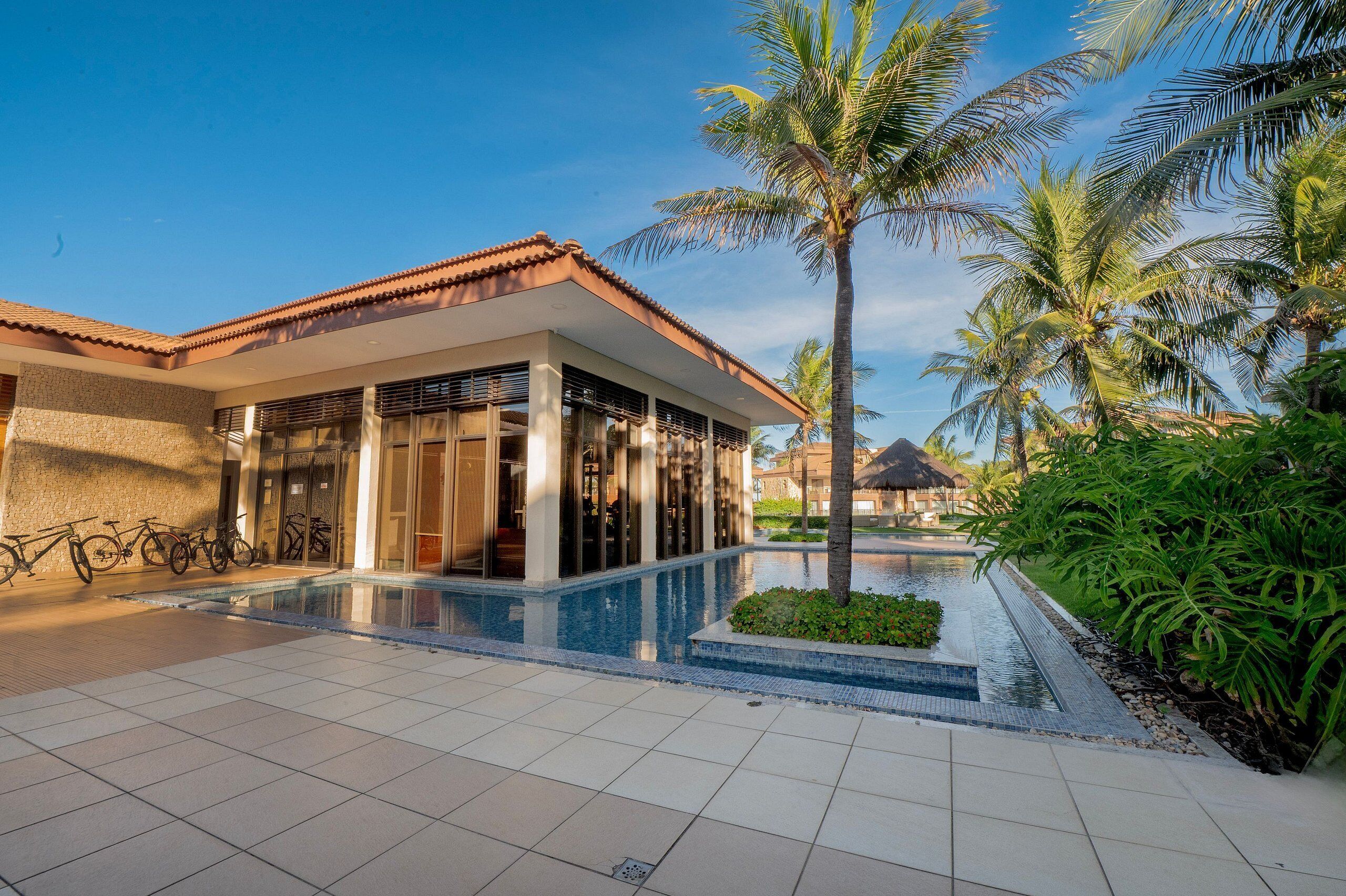 Un resort con piscina, palmeras y un edificio de amplios ventanales.