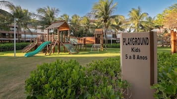 Ein Spielbereich mit Rutsche und Klettergerüsten, umgeben von Palmen und Grünpflanzen.