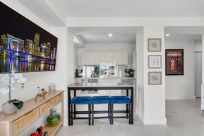 A modern kitchen with white cabinets, a central island, and blue bar stools. - South Beach 1BR on Ocean Drive · Steps to the Sand (Miami Beach)