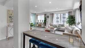 Una sala de estar moderna con una mesa de comedor de mármol, un conjunto de sofás y un ventanal con vistas a edificios.