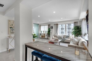 A modern living room with a marble dining table, a sofa set, and a large window with a view of buildings. - South Beach 1BR on Ocean Drive · Steps to the Sand (Miami Beach)