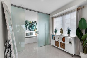 A modern interior with a sliding glass door leading to a bedroom, a white console table with decorative items, and a large window with curtains. - South Beach 1BR on Ocean Drive · Steps to the Sand (Miami Beach)