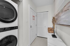 A laundry room with two washing machines, a door with a fire exit sign, and a decorative wall piece. - South Beach 1BR on Ocean Drive · Steps to the Sand (Miami Beach)