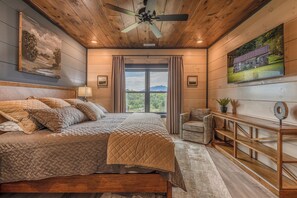 Ein Schlafzimmer mit einem großen Bett, einem Deckenventilator, einem Fenster mit Vorhängen und Blick ins Freie.