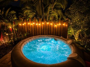Ein Whirlpool, umgeben von einem Holzzaun mit Lichterketten, inmitten eines tropischen Gartens bei Nacht.
