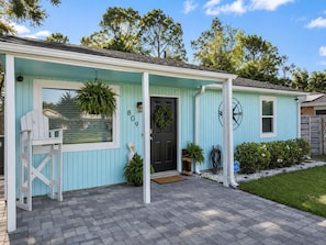 A light blue house with a black door, number 809, and a porch with a white chair. - Sandy Beach Days + Saltwater Poolside Nights (Pensacola)