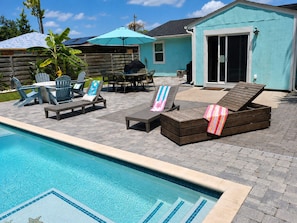 A backyard with a swimming pool, lounge chairs, a table with chairs, and a covered patio area. - Sandy Beach Days + Saltwater Poolside Nights (Pensacola)