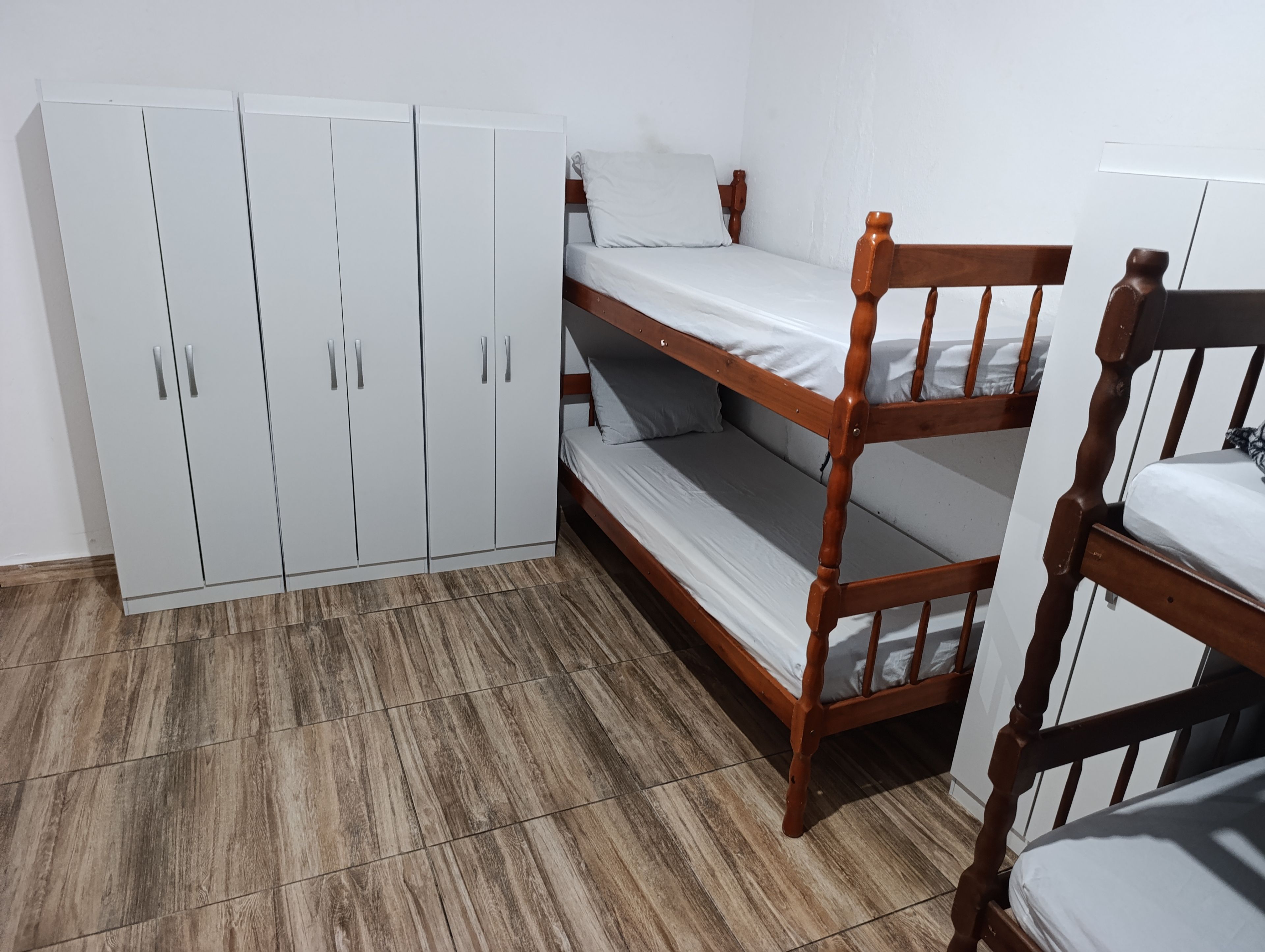 Ein Stockbett mit Holzrahmen und weißer Bettwäsche, ein weißer Kleiderschrank mit silbernen Griffen und ein Holzboden.