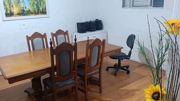 A dining area with a wooden table and chairs, a television on a cabinet, and a vase with sunflowers.