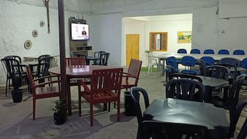 An indoor dining area with tables and chairs, a television, and a door leading to another room.