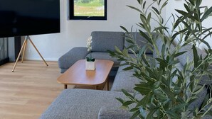 A modern living room with a grey sofa, a wooden coffee table, and a large window with a view of greenery.